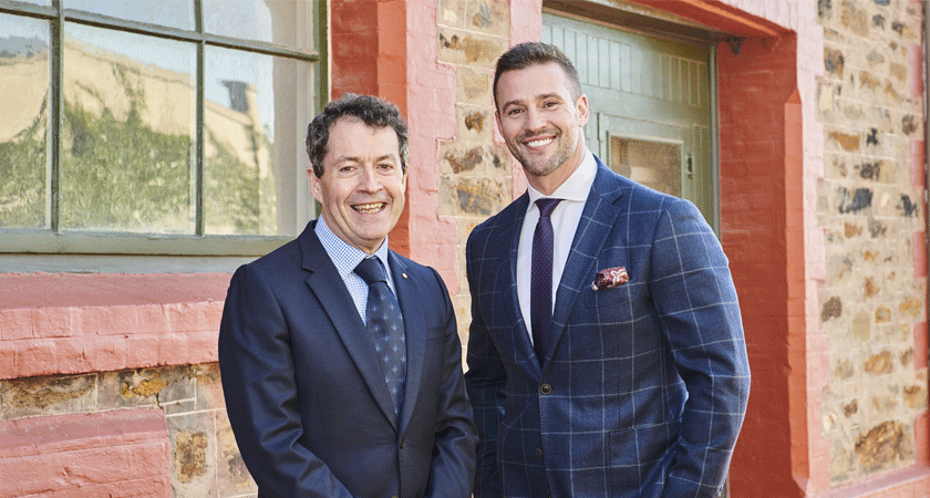 Peter Gago and Kris Smith stand against heritage brick building